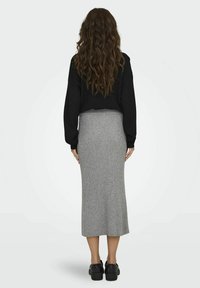 Sudadera negra corta combinada con una falda midi gris ajustada con canalé, complementada con unos zapatos negros resistentes, vista desde la parte de atrás.
