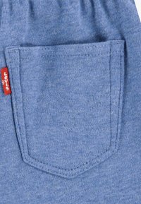 Tessuto di cotone blu con un dettaglio della tasca caratterizzato da un design cucito e un'etichetta rossa Levis. La texture è liscia, con una finitura morbida.
