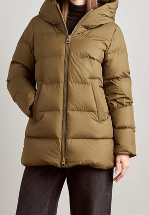 Doudoune matelassée vert olive avec capuche, fermeture éclair à l'avant et poches latérales, portée sur un top noir et un pantalon foncé.