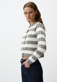Grau-weiß gestreiftes, kurzes Strickjäckchen aus weichem Material, mit rundem Ausschnitt und drei Knöpfen auf der Vorderseite.