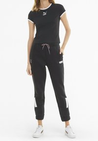 Czarna koszulka z białym obszyciem i logo Puma; czarne spodnie dresowe ze sznurkiem w pasie, bocznymi kieszeniami i białymi akcentami przy mankietach; białe sneakersy.