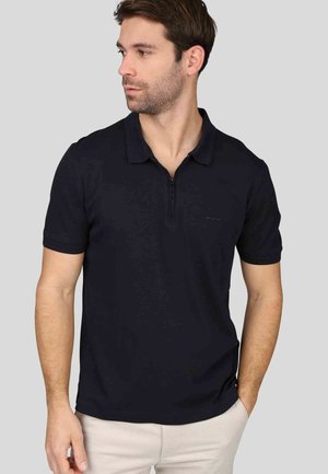 Chemise polo marine avec une courte fermeture éclair, texture douce et surpiqûres contrastantes. Conçue avec des manches courtes et un col classique.
