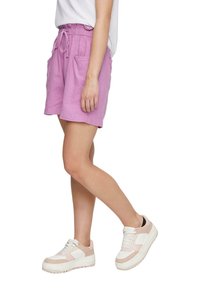 Shorts en lin roses avec une taille élastique et un cordon de serrage, dotés de deux poches latérales. Portés avec des baskets blanches et roses.
