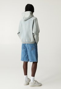 Svijetloplava hoodie sa opuštenim krojem, uparena s traper kratkim hlačama. Hlače imaju džep s malim brend logom. Bijele čarape i bež tenisice.