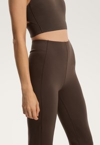 Rjave atletske leggins hlače z visokim pasom in gladko teksturo. Imajo vertikalne šive za eleganten videz. Ujemajoče se doprsje.