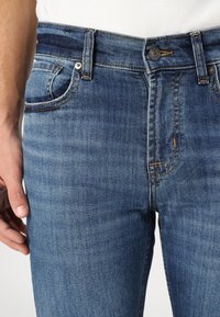 Light blue denim jeans with a fitted shape, featuring a stitched waistband, front pockets, and subtle fading near the thighs.