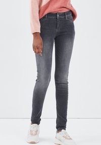 Vaqueros ajustados grises de mezclilla, con un leve desgastado, diseño estándar de cinco bolsillos y cierre de botón en la cintura.