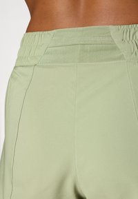 Pantaloni sportivi verdi con una cintura elastica testurizzata, tessuto liscio e cuciture pulite evidenziate nella vista posteriore.