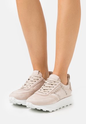 Sneakers de gamuza en color beige claro, con tachuelas decorativas en el lado, suela blanca y diseño de cordones tradicional.