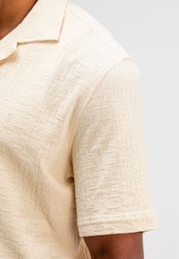 Korte mouwen polo shirt in lichtbeige met textuurstof, voorzien van een subtiel patroon en een klassiek kraagontwerp.