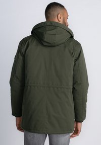 Chaqueta aislante verde oliva con capucha, que presenta un corte recto, puños elásticos y sutiles detalles de costura en la parte posterior.