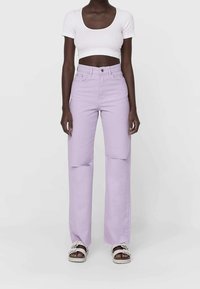 Jeans de lavanda de tiro alto con piernas anchas, que presentan dos desgastados en las rodillas y una textura suave, combinados con un top corto de rayas blancas y sandalias.
