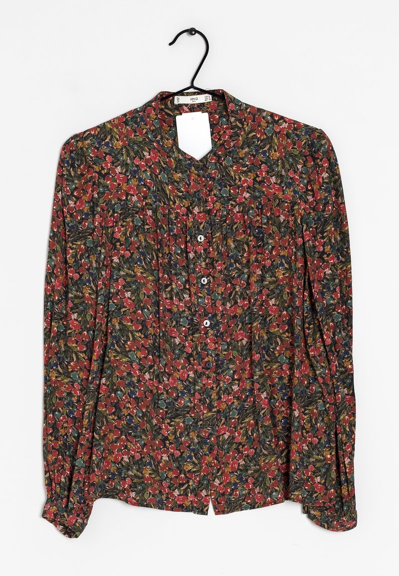 Chemise à manches longues avec un motif floral rouge, vert et jaune suspendue sur un cintre noir contre un fond blanc.