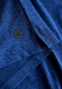 Blaues Sportshirt aus strukturiertem Stoff, mit einem kleinen schwarzen Logotag und genähten Saumdetails.