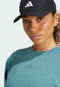 Teal sweatshirt with a textured logo in front; black cap featuring white logo. Smooth fabric texture and casual design.