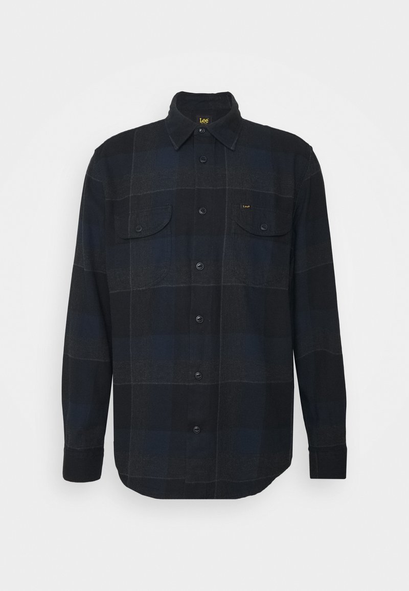 Chemise à carreaux noire et bleu foncé à manches longues, boutonnée, avec col et deux poches poitrine, présentée sur un fond clair uni.
