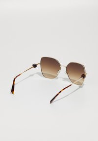 Occhiali da sole con forma esagonale, lenti a gradiente marrone, montatura in metallo dorato e steli con motivo tartarugato e dettagli trasparenti.