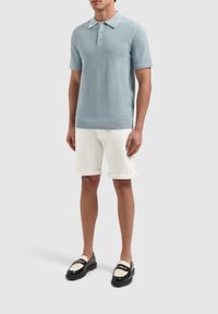 Lichtblauwe gebreide polo met korte mouwen, drieknopenlijst, gecombineerd met opgerolde witte denimshorts en zwarte instappers.