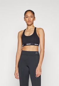 Sutiã esportivo preto com faixa logo DKNY, apresentando um decote em forma de gota e design de costas nadador. Combinado com leggings pretas de cintura alta.