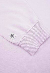 Ljuslila sweatshirttyg med ribbad mudd; har en vävd etikett med svart text på en vit fyrkant. Slät textur.
