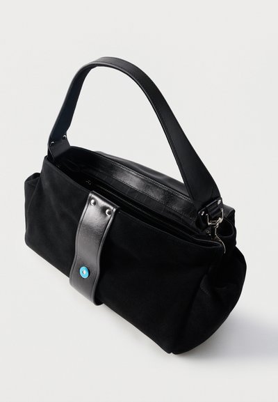 Μαύρη σουέντ τσάντα χειρός με φαρδιά δερμάτινη τιράντα, κλείσιμο με φερμουάρ και διακοσμητικό δερμάτινο πινακίδα με μικρή μπλε λεπτομέρεια κουμπιού.