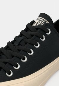 Black canvas sneaker with round toe, rubber sole, and metal eyelets. Features distinct lace-up design and textured fabric upper.