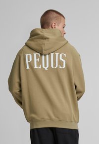 Khaki hoodie with a large white "PEQUS" text on the back. Features a drawstring hood and ribbed cuffs and hem. Smooth texture.