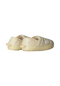 Zapatillas de casa acolchadas de color beige claro con forma redondeada, forro interior suave y suela de goma antideslizante. Presentan un logo y una pestaña de tirón en la parte trasera.