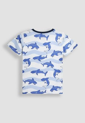 T-shirt à manches courtes en bleu clair avec un motif de requin dans différentes nuances de bleu marine et des vagues. Matière en coton, design col rond.