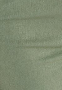 Tessuto verde chiaro con un pattern tessuto e testurizzato. Il materiale ha un aspetto morbido e una tonalità di colore leggermente attenuata.