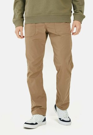 Beige, leichte Hose mit glatter Textur, flachen Fronttaschen und schmal zulaufenden Beinen, kombiniert mit weißen Sneakers mit marineblauen Akzenten.