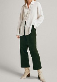 White long-sleeve shirt with a textured front panel, paired with dark green corduroy wide-leg pants and cream ankle boots.
