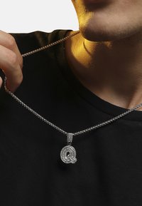 Sølv kæde med et cirkulært vedhæng, der har et dekorativt bogstav "Q" besat med funklende rhinsten.