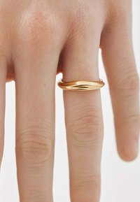 Anillo de oro en un dedo, con una superficie lisa y pulida que presenta un sutil diseño de ondas. La textura de la piel es visible en la mano.