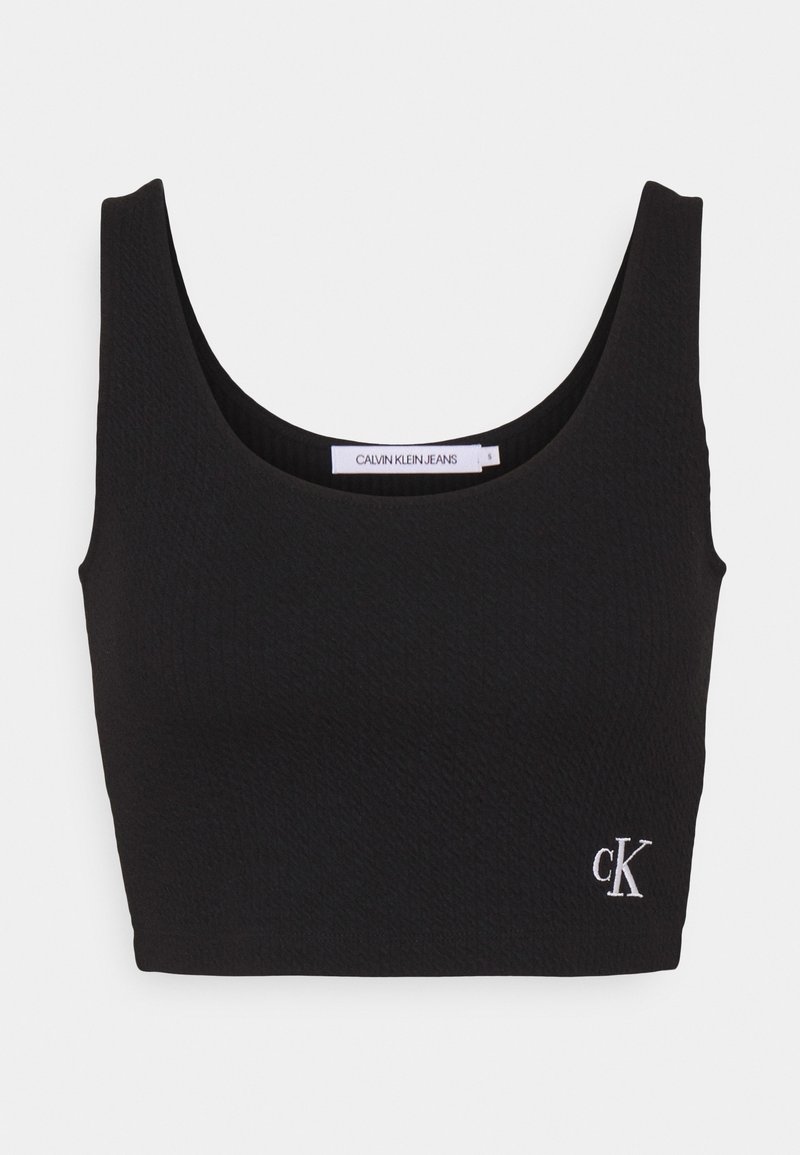 Top court noir côtelé avec un décolleté arrondi et un petit logo blanc "ck" sur le côté gauche. Confectionné dans un matériau texturé et flexible.
