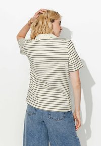 Polo beige à rayures avec des manches courtes. Doté d'un col classique et d'un tissu texturé. Associez-le à un jean ample bleu clair.