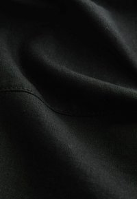 Gros plan sur un tissu noir montrant une texture subtile et des détails de couture avec des plis doux et des ombres.