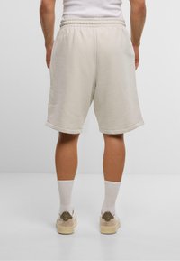 Svetlo béžové bavlnené šortky s elastickým pásom, srolovanými okrajmi a decentnou výšivkou na ľavej nohe. Nosia sa s bielymi ponožkami a teniskami.