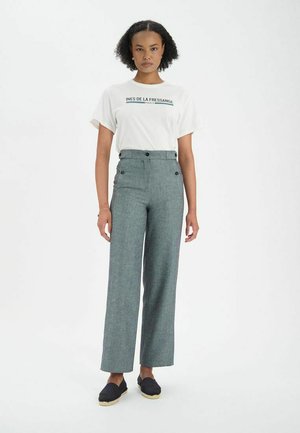 T-shirt blanc avec l'imprimé "INES DE LA FRESSANGE PARIS", associé à un pantalon taille haute, large, de couleur gris-bleu avec deux détails de bouton.