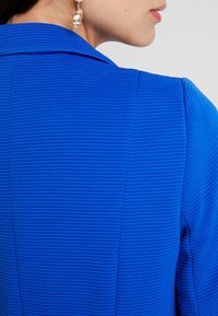 Niebieska ribbed kurtka z usztywnionym kołnierzem, z teksturowanymi pionowymi liniami, dopasowanym krojem i widocznymi detalami szwów.