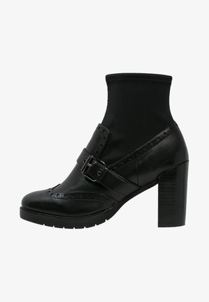 Botines negros con un tacón alto y grueso, material de cuero, parte superior elástica tipo calcetín, hebilla decorativa y detalles de brogue en la puntera.