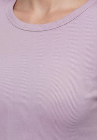 Gros plan d'une personne portant un haut en tissu côtelé violet clair avec un col arrondi.