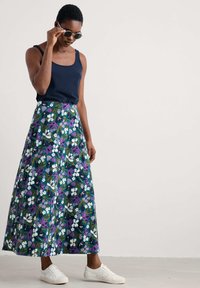 Floral maxi skirt in dark teal with white and purple flower patterns. Paired with a navy tank top and white sneakers.