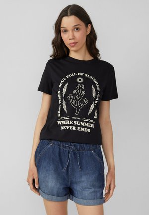 T-shirt en coton noir à manches courtes, avec un motif graphique blanc de feuillage et du texte centré à l'avant. Associé à un short en denim.