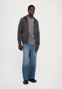Gray zip-up hoodie, gray t-shirt, wide blue jeans, and black shoes; casual outfit with soft fabric and relaxed fit.