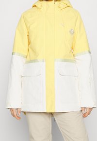 Gelbe und weiße wasserdichte Jacke mit Kapuze, zwei Fronttaschen, gemusterten Akzenten an den Ärmeln und einem Logodetail.