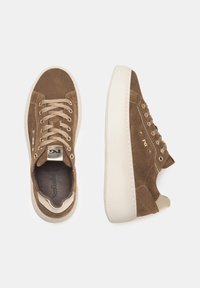 Sneaker in suede marrone con accenti beige, punta rotonda, suola in gomma e lacci piatti. Presenta un logo metallico sulla linguetta e sul lato.