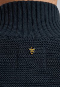 Donkerblauwe gebreide trui met een geribde hoge kraag, een textuur in het lichaam en een gouden embleem met "PME Legend" aan de zijkant.