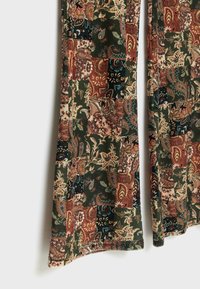 Tissu patchwork à motif cachemire avec des motifs floraux et de feuilles verts, rouille, beige et bleu foncé sur les jambes du vêtement.