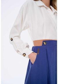 Biała bluzka z kołnierzykiem i plisowaną niebieską spódnicą. Złote guziki przy mankietach i w pasie, beżowy akcent w pasie, boczne kieszenie w spódnicy.